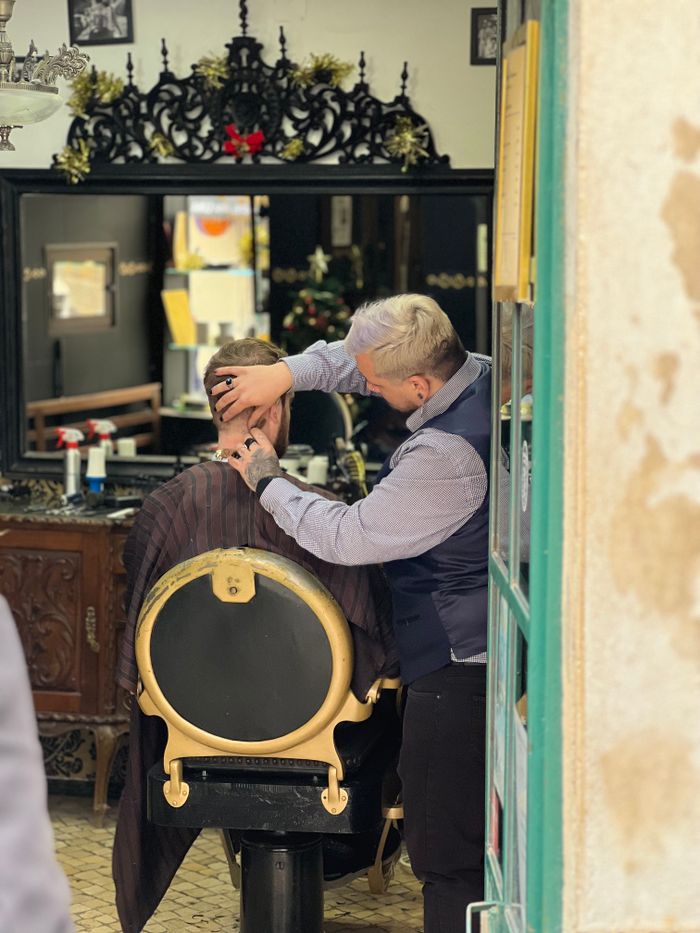 A barber carefully cuts a customer's hair in a traditional Lisbon barbershop, creating a classic look.