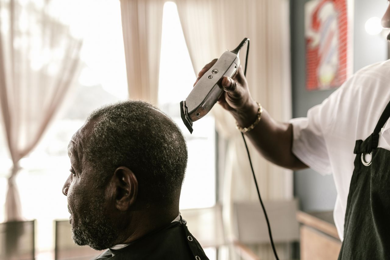Barber using clippers to give a haircut in a modern barber shop, side view.