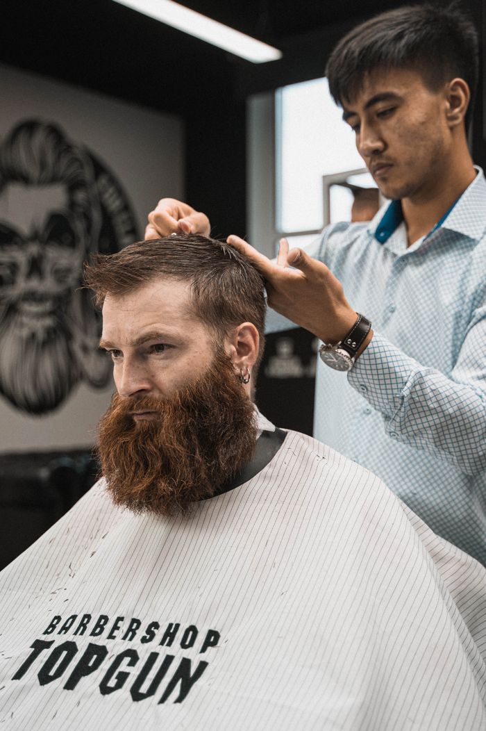 A man with a beard getting a haircut at a modern barber shop by a hairstylist.